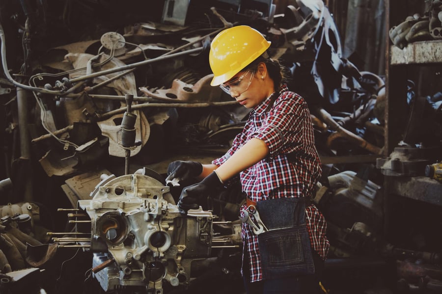 A women with a yellow hard hat working on an engine in a heavy manufacturing facility