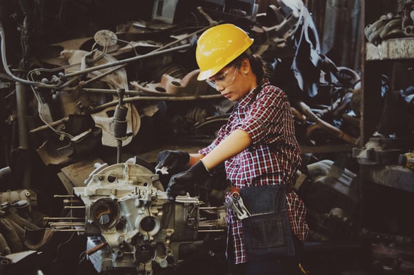 A women with a yellow hard hat working on an engine in a heavy manufacturing facility